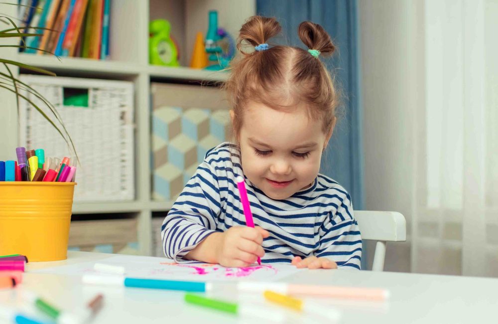 A beautiful little girl sits at a table at home and draws. Development of preschoolers.